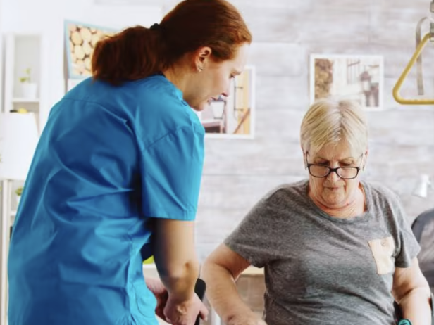 Eine Pflegefachperson der private Spitex hilft einer älteren Frau beim Aufstehen in einem häuslichen Umfeld – ein Moment praktischer Unterstützung und Fürsorge. Das Bild illustriert die wichtige Rolle privater Spitex-Organisationen in der alltäglichen Betreuung und Hauswirtschaft. Im Kontext des Blogs zur Mehrwertsteuerbefreiung zeigt es, wie die IAHA (International Association for Healthy Aging) sich für faire Rahmenbedingungen und die Gleichbehandlung privater Spitex-Leistungen in der Schweiz starkmacht.